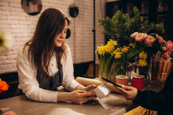 Plan recadré de fleuriste femelle tenant smartphone payer pour les fleurs dans le magasin de fleurs - Photo, image