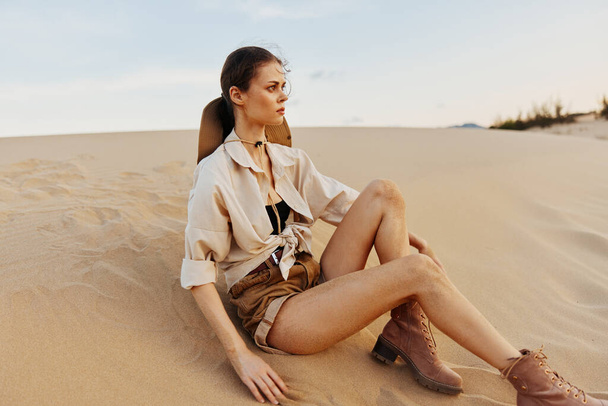 Mujer sentada en la duna de arena con camisa blanca y botas marrones en el paisaje del desierto Concepto de aventura al aire libre - Foto, imagen