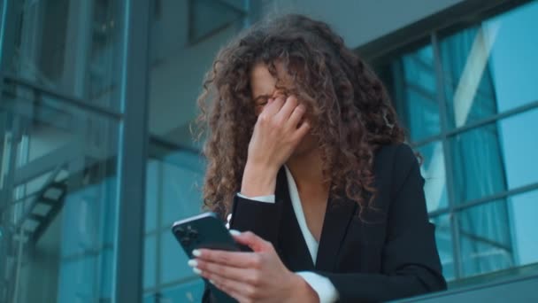 Tired Caucasian business woman girl businesswoman exhausted unwell ill girl hold smartphone looking at mobile phone screen feel pain rubbing dry eyes eyestrain headache blurry vision outdoors in city - Кадри, відео