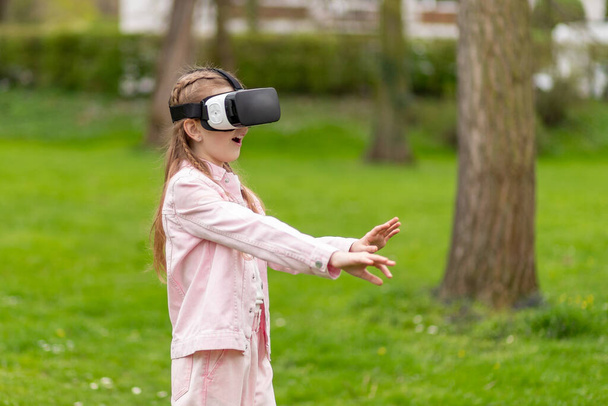 Klein meisje interacteert met virtual reality in park. - Foto, afbeelding