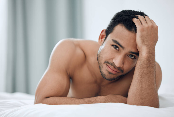 Morning, portrait and man lying in bed with confidence for relax, wellness and wakeup in bedroom. Home, body and Asian male person with muscles for resting, comfortable or weekend break in apartment. - Photo, Image