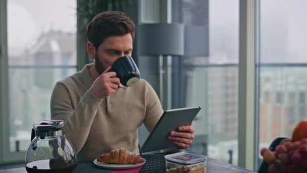 Пити працівник перегляду планшетного мислення робочих завдань у великих вікнах кухня крупним планом. Серйозний чоловік фрілансер читає електронну книгу, сіючи ранкову каву. Pensive бізнесмен дивиться комп'ютерні новини наодинці  - Кадри, відео