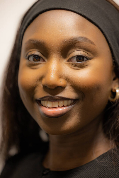 This image features a close-up portrait of a smiling Black woman wearing a black headband. Her dark, expressive eyes and radiant smile are the focal points of the image, highlighting her natural - Foto, imagen