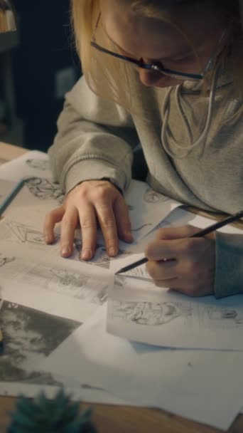 若い女性は,ホームベースのデザインスタジオでストーリーボードで働いています. テーブルの上にラップトップと静止した瓶. 女性はビデオのロードマップとしてスケッチを描きます. プリプロダクション。 バーティカルショット. - 映像、動画