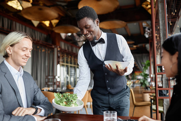 Ritratto di giovane uomo nero come cameriere che porta cibo sul vassoio per una cena in un ristorante di lusso - Foto, immagini