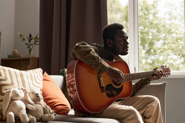 Side view portré felnőtt fekete férfi gitározik hangulatos otthon nyugodt földi hangok, másolás tér - Fotó, kép