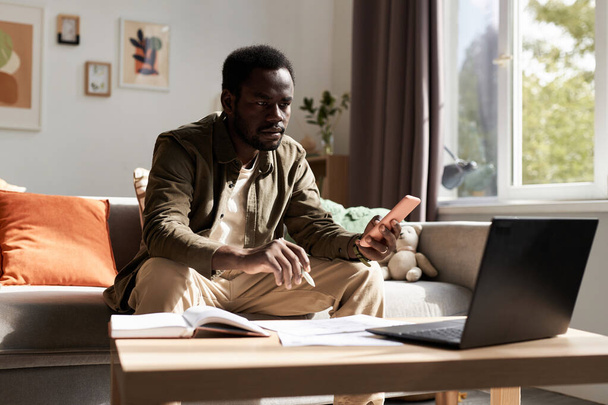 Πορτραίτο του ενήλικου μαύρου άνδρα που εργάζεται από το σπίτι και χρησιμοποιεί φορητό υπολογιστή στο φως του ήλιου, αντίγραφο χώρου - Φωτογραφία, εικόνα