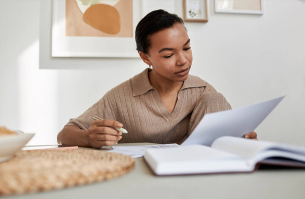 Minimális portré fiatal fekete nő olvasás dokumentumot otthon, miközben tanul, vagy csinál adót, másolás tér - Fotó, kép