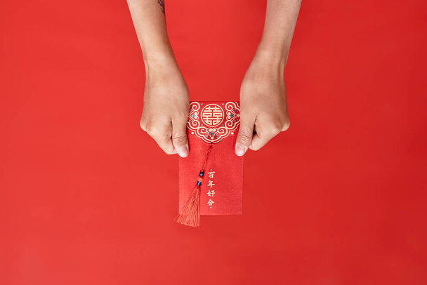 Крупним планом жіночі руки, що тримають конверт Хонбао на червоному тлі, як китайська новорічна традиція, копіювання простору Переклад Мають надлишок сотні років - Фото, зображення
