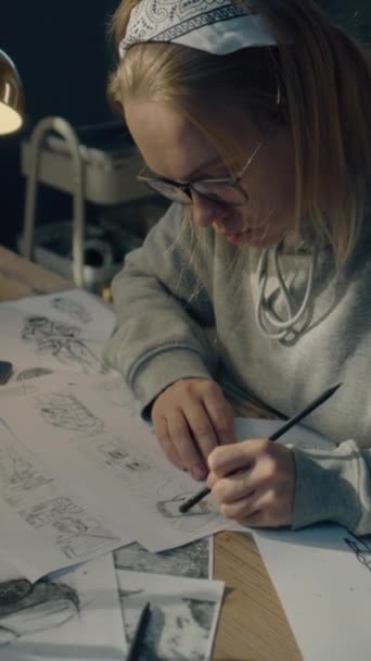 Γυναίκα animator δημιουργεί σκίτσα για το καρτούν. Κοιτάζει την οθόνη του λάπτοπ μπροστά της και ζωγραφίζει στο χαρτί. Συλλογή Κόμικς. Σκηνοθεσία ταινίας για προπαραγωγή. Κάθετη βολή. - Πλάνα, βίντεο