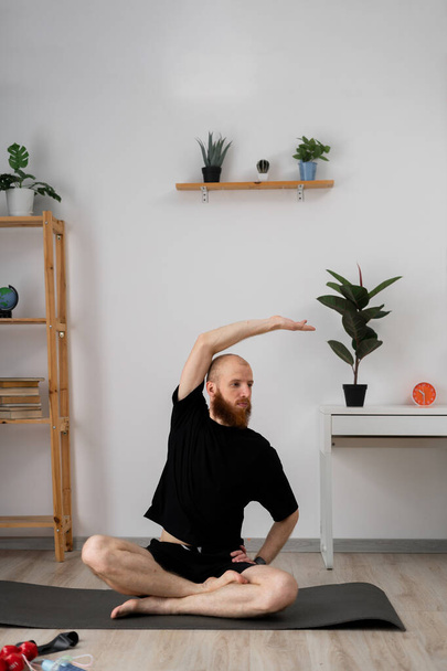 Brodaty mężczyzna uprawiający jogę rozciąga się w nowoczesnym, minimalistycznym salonie z roślinami dla spokojnej atmosfery - Zdjęcie, obraz