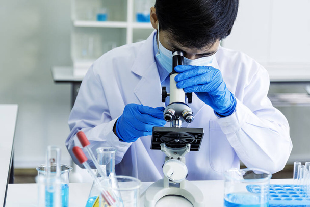 A tudósok kutatják a mikroszkóp kutatásait a tudományos laborban. Ázsiai tudós megnézi mikrobiológia mikroszkóp laboratóriumi berendezések kémiai labor. Biokémiai kutatási kísérleti vakcina koncepciója - Fotó, kép
