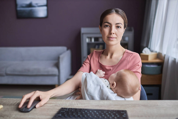 Front view POV of young working mother using computer with sleeping baby in arms,copy space - Photo, Image