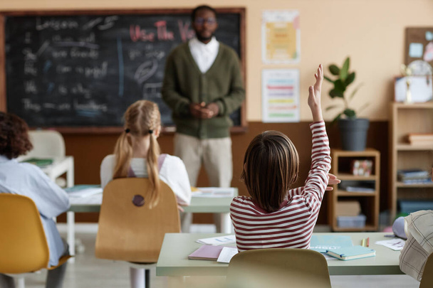 Valikoiva tarkennus laukaus tunnistamaton poika istuu pöydällä luokkahuoneessa nostamalla käsi Englanti luokassa, kopioi tilaa - Valokuva, kuva