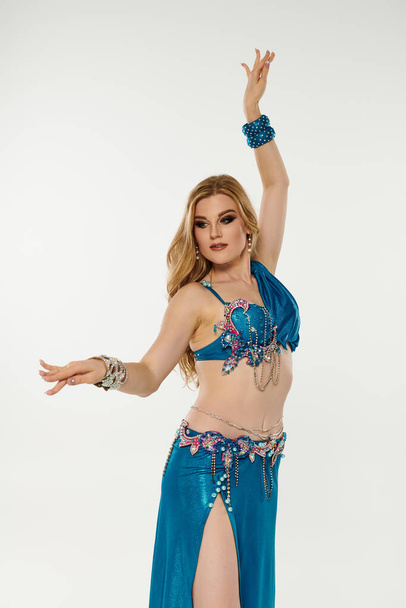Mujer joven cautivadora en un vibrante traje de danza azul del vientre mostrando sus movimientos elegantes. - Foto, imagen