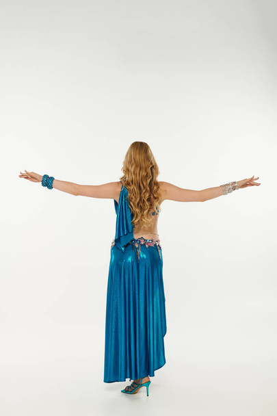 Young woman in a blue dress with arms outstretched while performing a belly dance. - Foto, imagen
