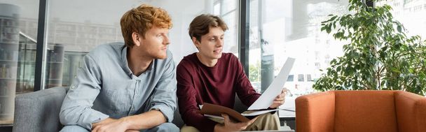 Two male students reviewing papers together on a couch. - Foto, immagini
