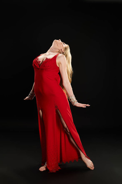 A young woman in a striking red dress strikes a graceful pose. - Photo, Image