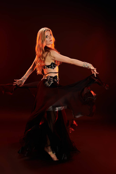 Young woman in black and white outfit gracefully belly dancing. - Photo, Image
