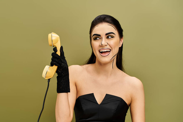 A pretty brunette woman, styled like pop art, clad in black dress, holding retro phone - Photo, Image