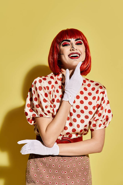Een mooie roodharige met pop art make-up, het aantrekken van een polka dot shirt en witte handschoenen op een levendige gele achtergrond. - Foto, afbeelding