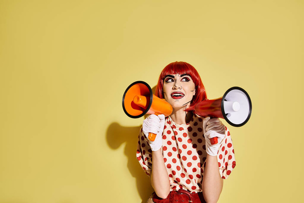 Uma mulher ruiva impressionante com maquiagem pop art segura um megafone contra um fundo amarelo vibrante. - Foto, Imagem
