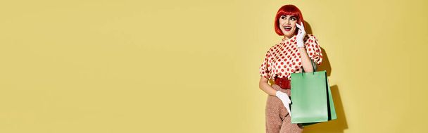 Hübsche rothaarige Frau steht mit grüner Einkaufstasche vor einer gelben Wand und präsentiert kreatives Pop-Art-Make-up. - Foto, Bild
