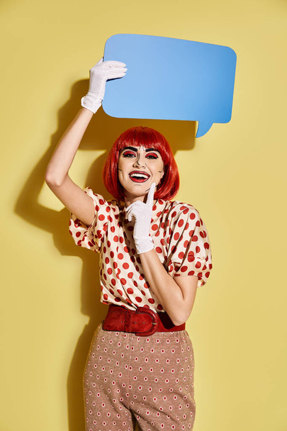 Een creatieve roodharige vrouw in polka dot blouse met een spraakbel boven haar hoofd op een gele achtergrond. - Foto, afbeelding