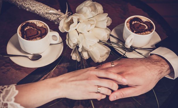 Δύο φλιτζάνια του καφέ και το χέρι της νύφης και του γαμπρού με βέρες - Φωτογραφία, εικόνα