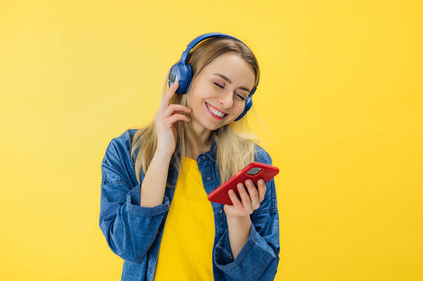 Mladá studentka pohled na chytrý telefon poslech hudby ve sluchátkách izolovaných na žlutém pozadí. - Fotografie, Obrázek