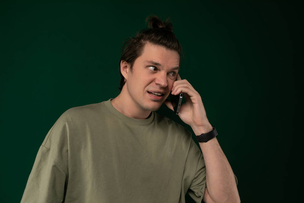 A young man is standing outdoors, engaged in a conversation on his cell phone. He is holding the phone up to his ear and appears focused on the call. - Photo, Image