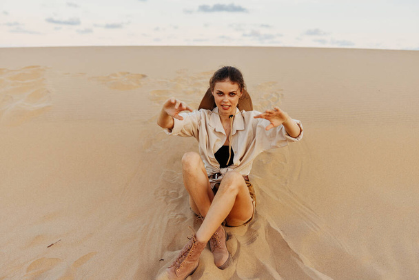 Femme assise au sommet d'une dune de sable avec les mains levées dans l'air, profitant d'un moment paisible et serein dans un désert sauvage - Photo, image
