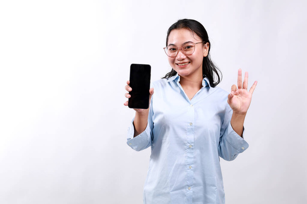 Muotokuva ihana nuori aasialainen liikenainen tilalla matkapuhelin ja osoittaa ok ele eristetty valkoisella taustalla - Valokuva, kuva
