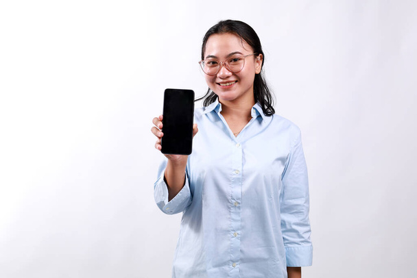 Attractive pleasant asian business woman present new phone app, hold smartphone show telephone screen, introduce application on display, stand white background delighted - Photo, Image