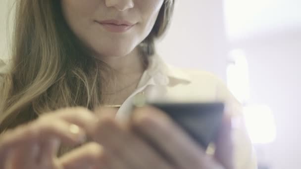 Młoda kobieta uśmiechający się trzymając telefon w ręku i surfowania w Internecie. - Materiał filmowy, wideo