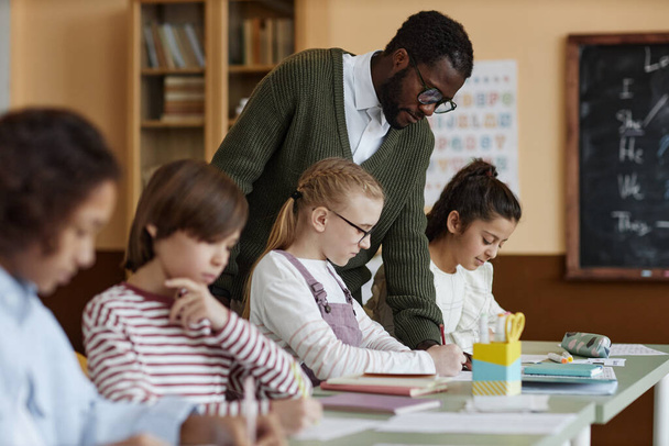 アフリカ系アメリカ人の男性教師 授業で働く英語の教師 子供が運動を書いているのを見る - 写真・画像