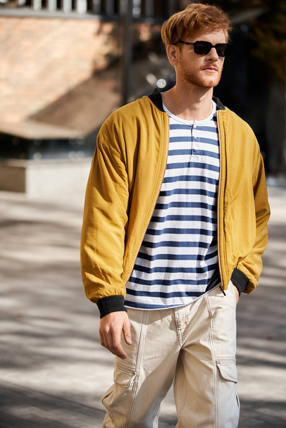 市街地を散策するスタイリッシュな黄色いジャケットの赤毛の男. - 写真・画像