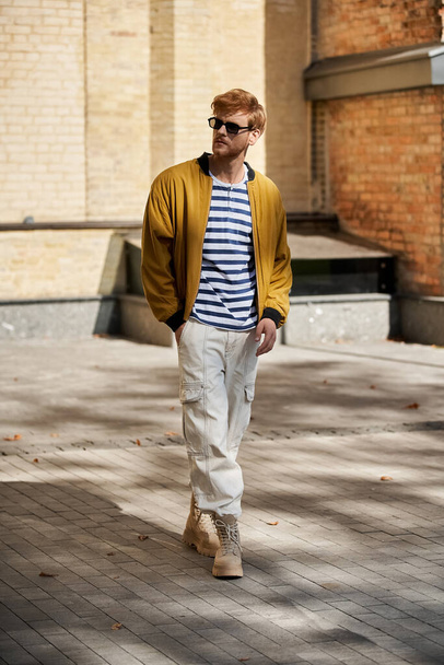 活気に満ちた黄色のジャケットで街の通りを散策するスタイリッシュな赤毛の男. - 写真・画像