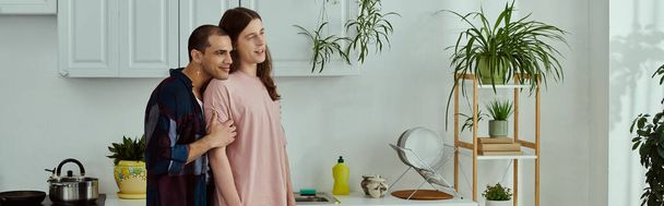 Ένα γκέι ζευγάρι με casual ρούχα που απολαμβάνουν ποιοτικό χρόνο μαζί, ενώ στέκεται σε μια ζεστή κουζίνα. - Φωτογραφία, εικόνα