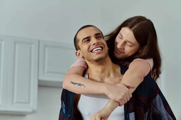 Muž v neformálních šatech drží něžně v náručí partnera, který sdílí intimní okamžik lásky a spojení. - Fotografie, Obrázek
