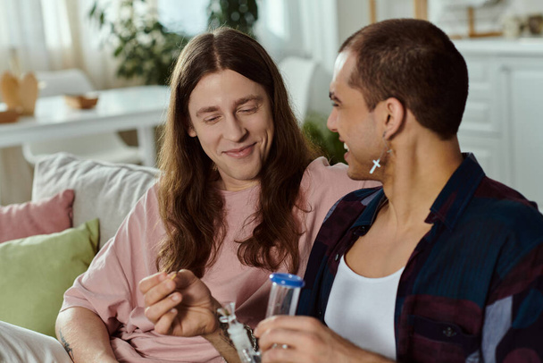 a gay couple, sit comfortably on a couch, enjoying each others company, lighting marijuana in the glass bong - Photo, Image