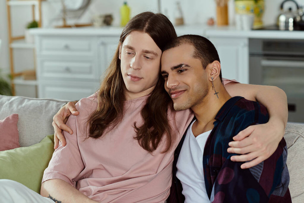 A gay couple in casual clothes sit closely on a couch, enjoying quality time together at home. - Фото, изображение