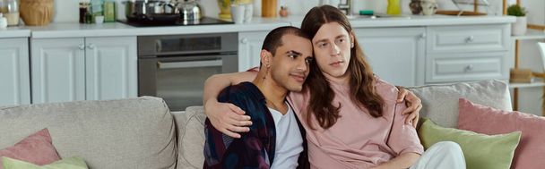 ένα γκέι ζευγάρι, που κάθονται κοντά σε έναν άνετο καναπέ, μοιράζονται μια στιγμή αγάπης και συντροφικότητας. - Φωτογραφία, εικόνα