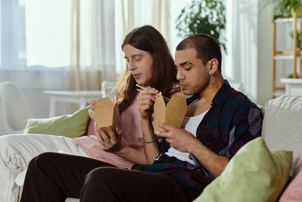 Una pareja gay en ropa casual pasando tiempo de calidad juntos, sentados en un sofá en un ambiente acogedor en casa. - Foto, Imagen