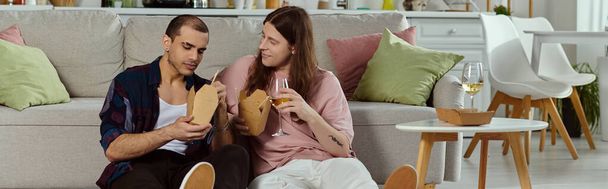 Um casal gay, em traje casual, relaxando em um sofá em um ambiente acolhedor, desfrutando de tempo de qualidade juntos. - Foto, Imagem