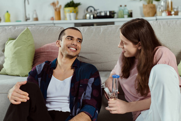 couple in casual attire enjoy a peaceful moment together on a cozy couch at home, holding glass bong - Photo, Image