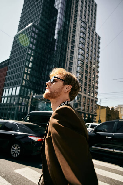 Junger rothaariger Mann geht anmutig neben hohen städtischen Gebäuden. - Foto, Bild