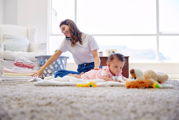 Mother, baby and phone call with toys for tummy time or playing on living room floor, carpet or blanket at home. Busy mom with laundry or conversation by little girl, infant or newborn for childcare. - Photo, Image