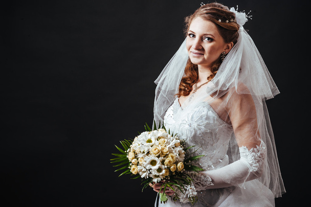 Fashion model with bridal bouquet drinking champagne and wearing wedding dress at black studio background - Photo, Image