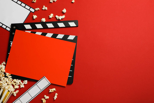 Clapperboard, taza de papel con palomitas de maíz, película y carrete sobre fondo rojo, espacio para texto - Foto, imagen